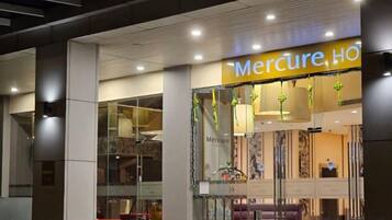 A hotel entrance with a prominent sign, a reception area with seating, and a glass facade.