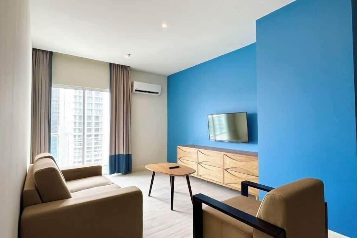 Un soggiorno moderno con un divano, un tavolino rotondo e una TV montata su una parete blu.