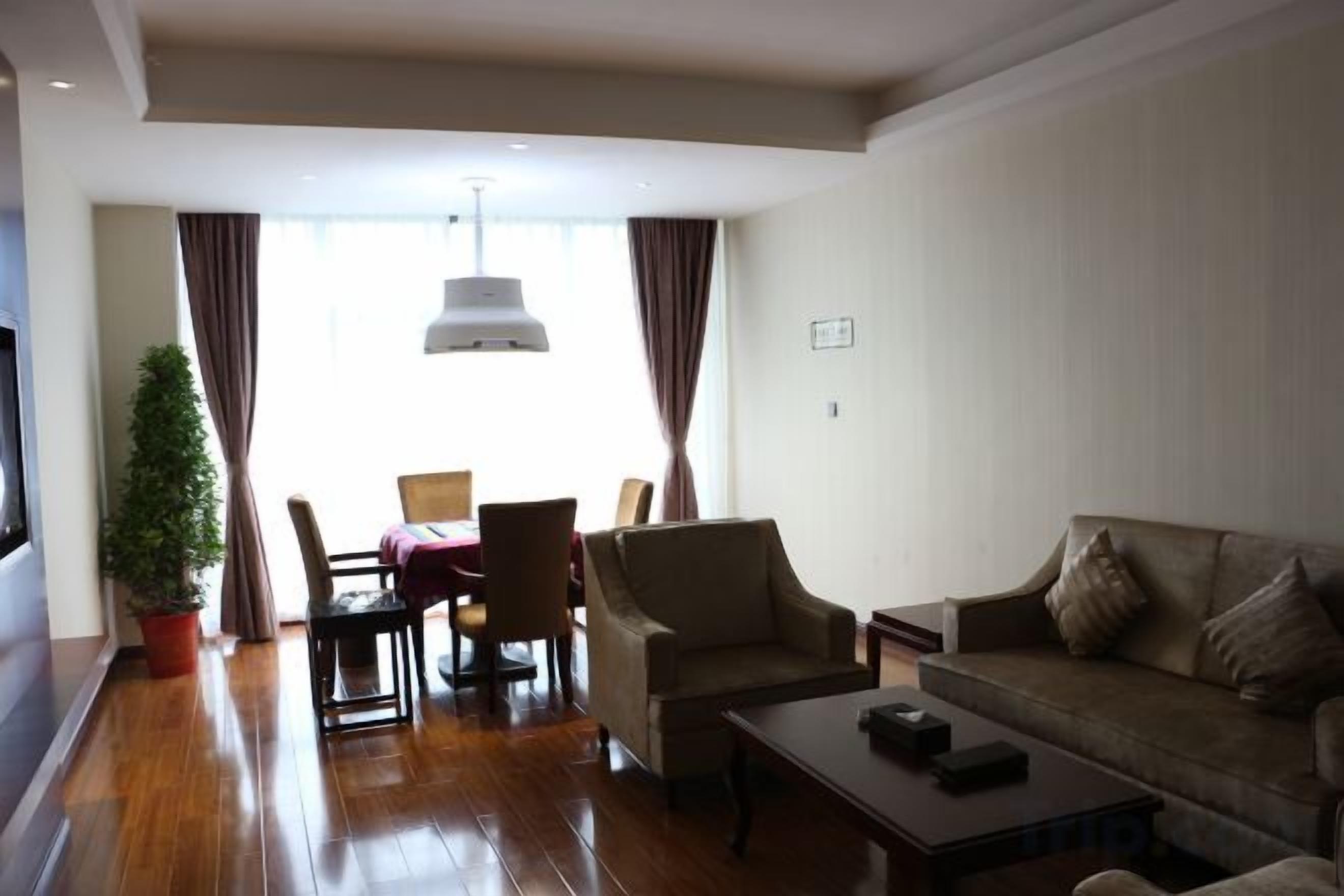 A hotel room with a wooden floor, a sofa, a coffee table, a TV, and a dining table with chairs.