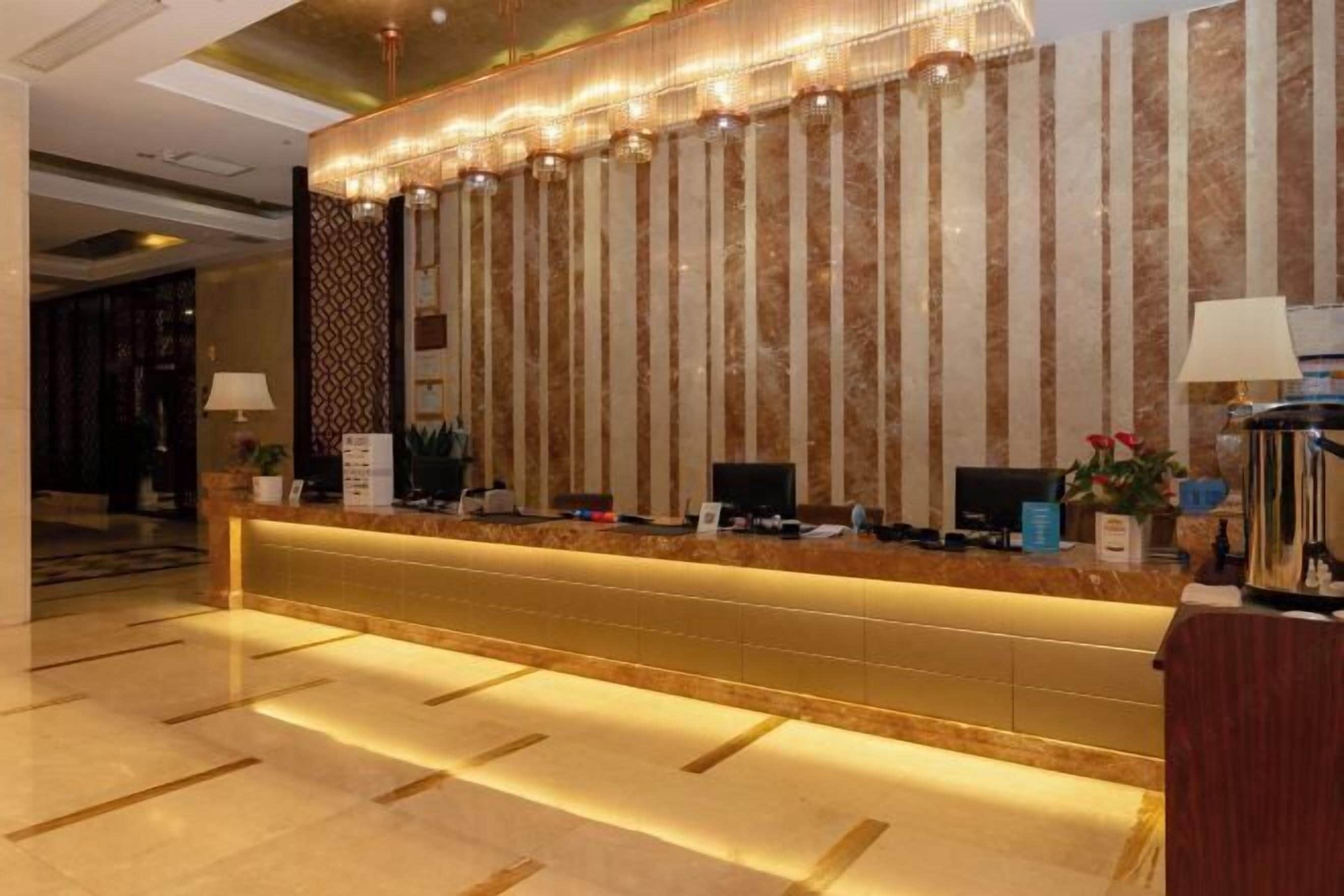 A hotel reception area with a marble counter, a patterned wall, and a modern chandelier.