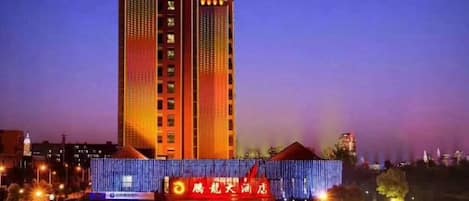 A tall hotel building with a modern design, featuring a prominent entrance with a red awning and illuminated signage.