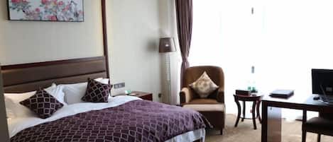 A hotel room with a large bed, a desk, a chair, and a television.