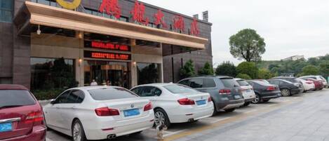 A building with a sign in a foreign language, a parking lot with several cars, and a tree in the background.