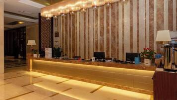 A reception desk with a marble wall, a flat-screen TV, and a plant.