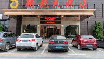 A hotel entrance with a clear sign, a parking lot with several cars, and a modern building facade.