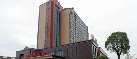 Hotel de varios pisos con una entrada destacada, estacionamiento y una pequeña estructura adyacente.