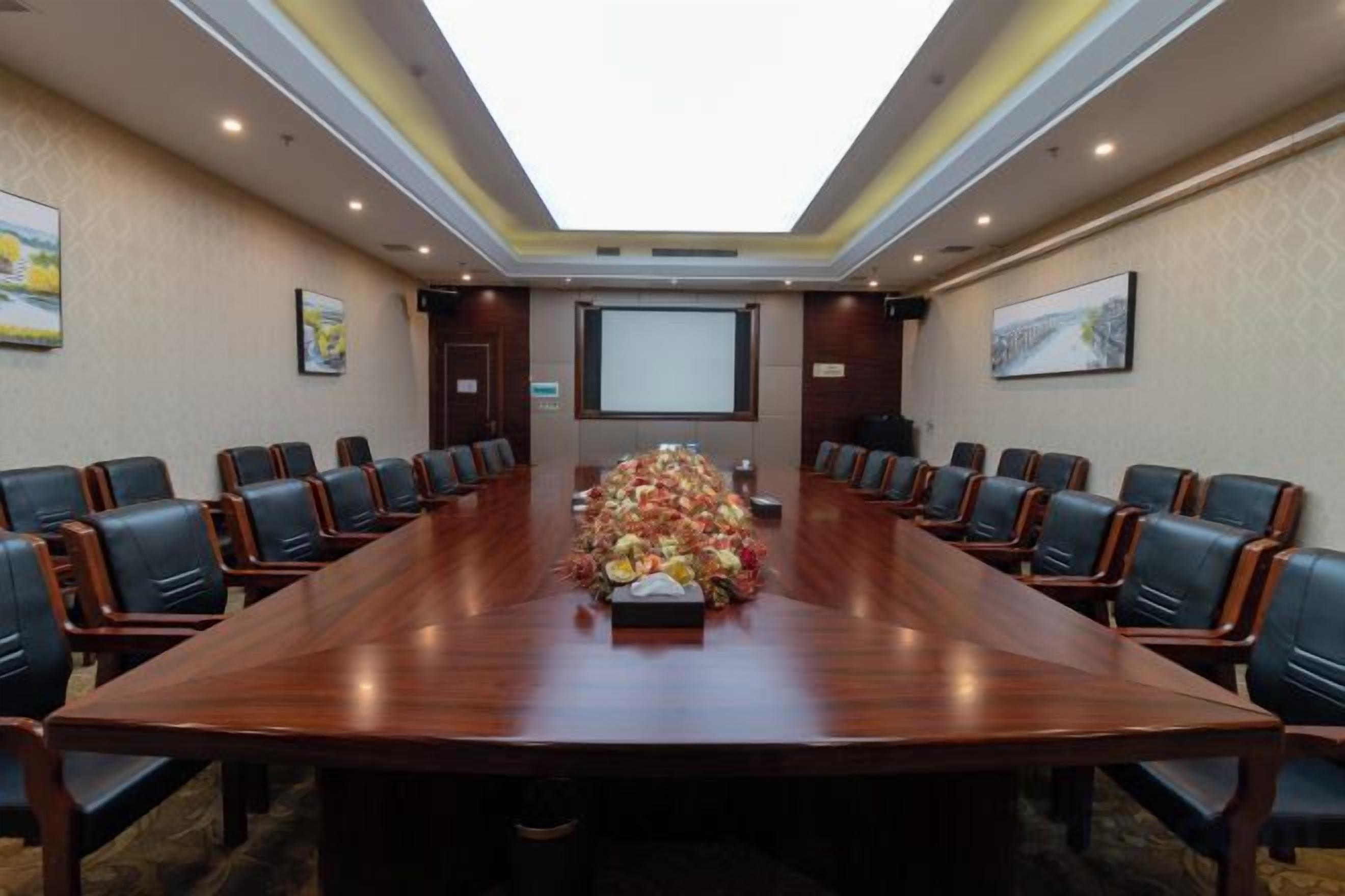Un salón de conferencias con una larga mesa, sillas, una pantalla de proyector y centros de mesa con flores.