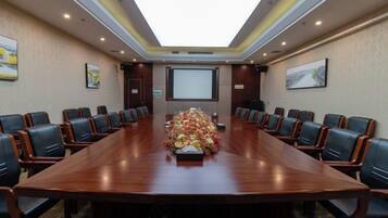 Un salón de conferencias con una larga mesa, sillas, una pantalla de proyector y centros de mesa con flores.