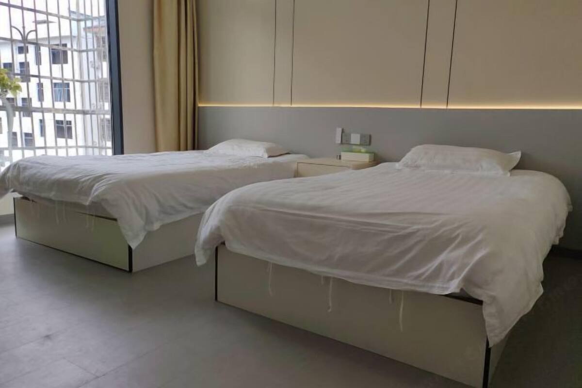 Habitación de hotel con dos camas, una mesita de noche y una ventana con vistas a edificios.