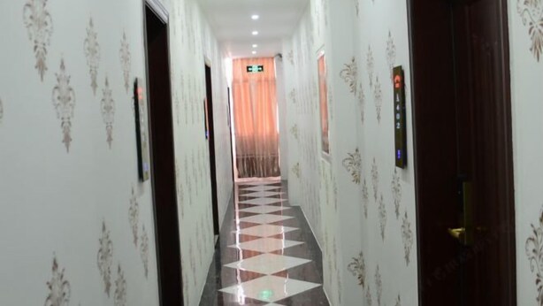 Um corredor de hotel com papel de parede estampado, chão xadrez e um elevador.