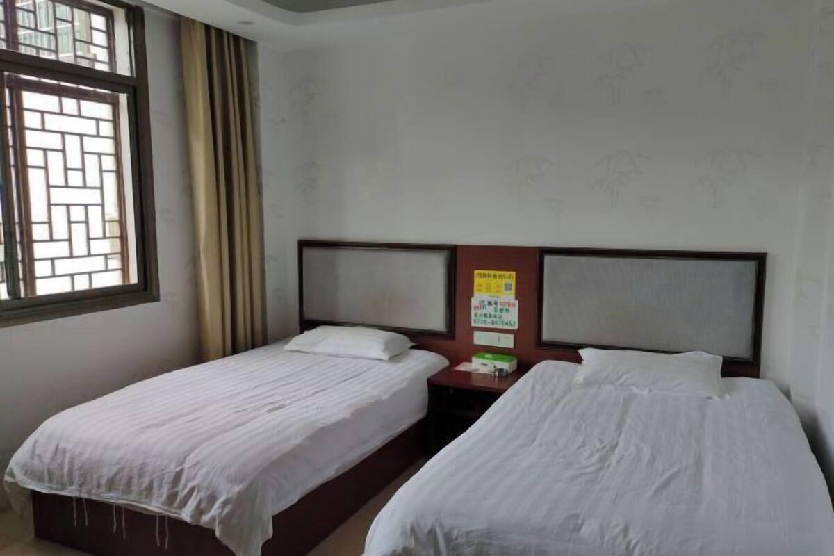 Una habitación con dos camas individuales, una ventana con cortinas y un tablón de anuncios en la pared.