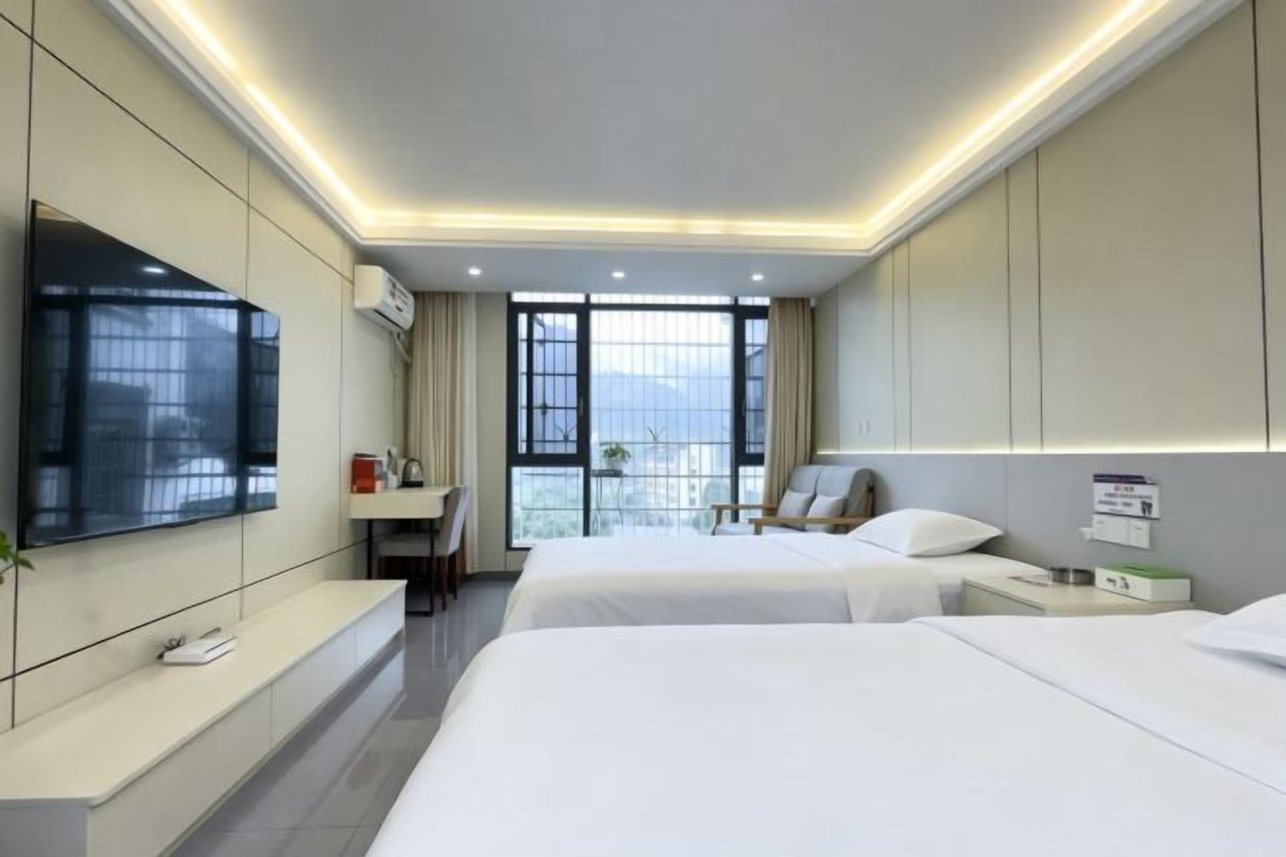 A hotel room with two beds, a TV, a desk, and a balcony with a view.