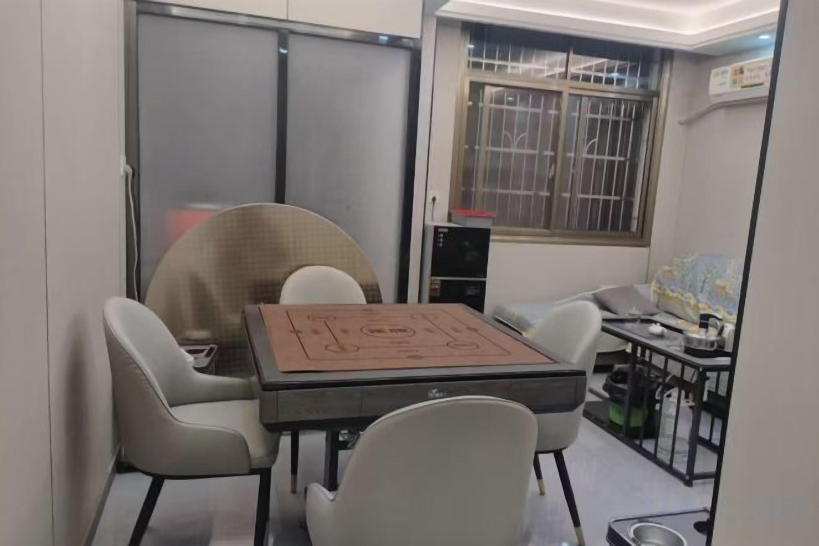 A compact room with a table and chairs, a window with bars, and a bed with a patterned bedspread.