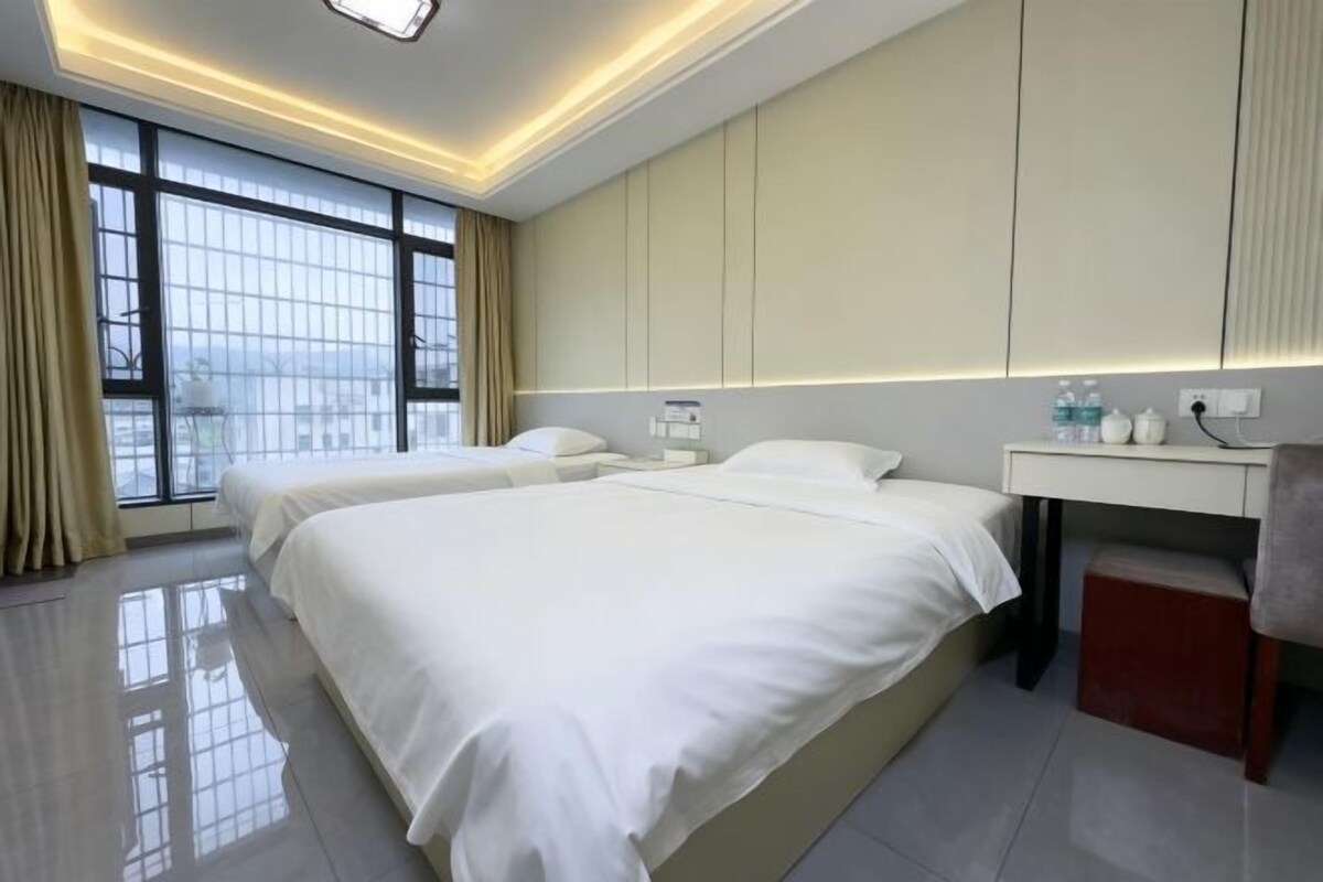 A hotel room with two beds, a bedside table, a desk, and a large window.