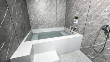 A modern bathroom with a freestanding bathtub, a handheld showerhead, and a control panel.