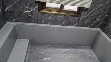 A bathroom with a marble floor, a window with blinds, and a tiled shower area.
