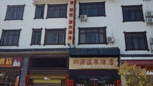 Fachada de hotel com várias janelas, uma placa vertical proeminente com caracteres chineses e uma loja no andar térreo com número de contato.