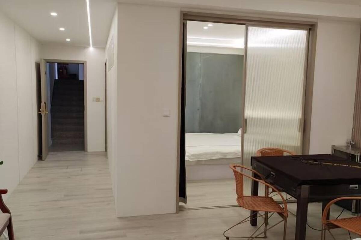 Una habitación de hotel con cama, una mesa de comedor con sillas, una puerta corredera al baño y una escalera que conduce a otra habitación.