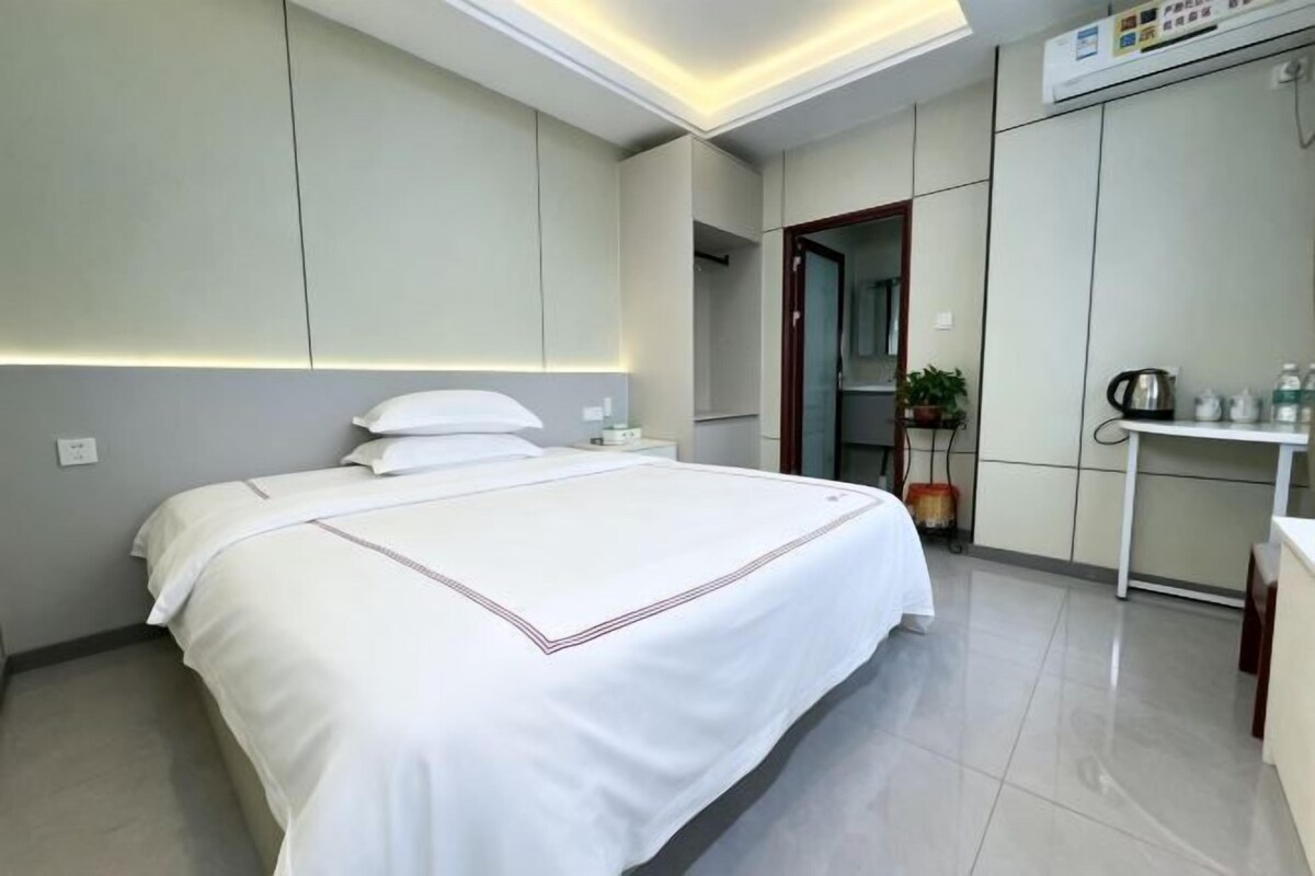 A hotel room with a large bed, bedside table, and a small desk with a chair.