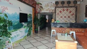 Um saguão de hotel com balcão de recepção, uma televisão fixada na parede e um mural retratando uma paisagem montanhosa.
