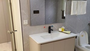 A bathroom with a white sink, a mirror, a toilet, and a trash bin. - Xiangyuan Hot Spring Hotel (Rucheng)