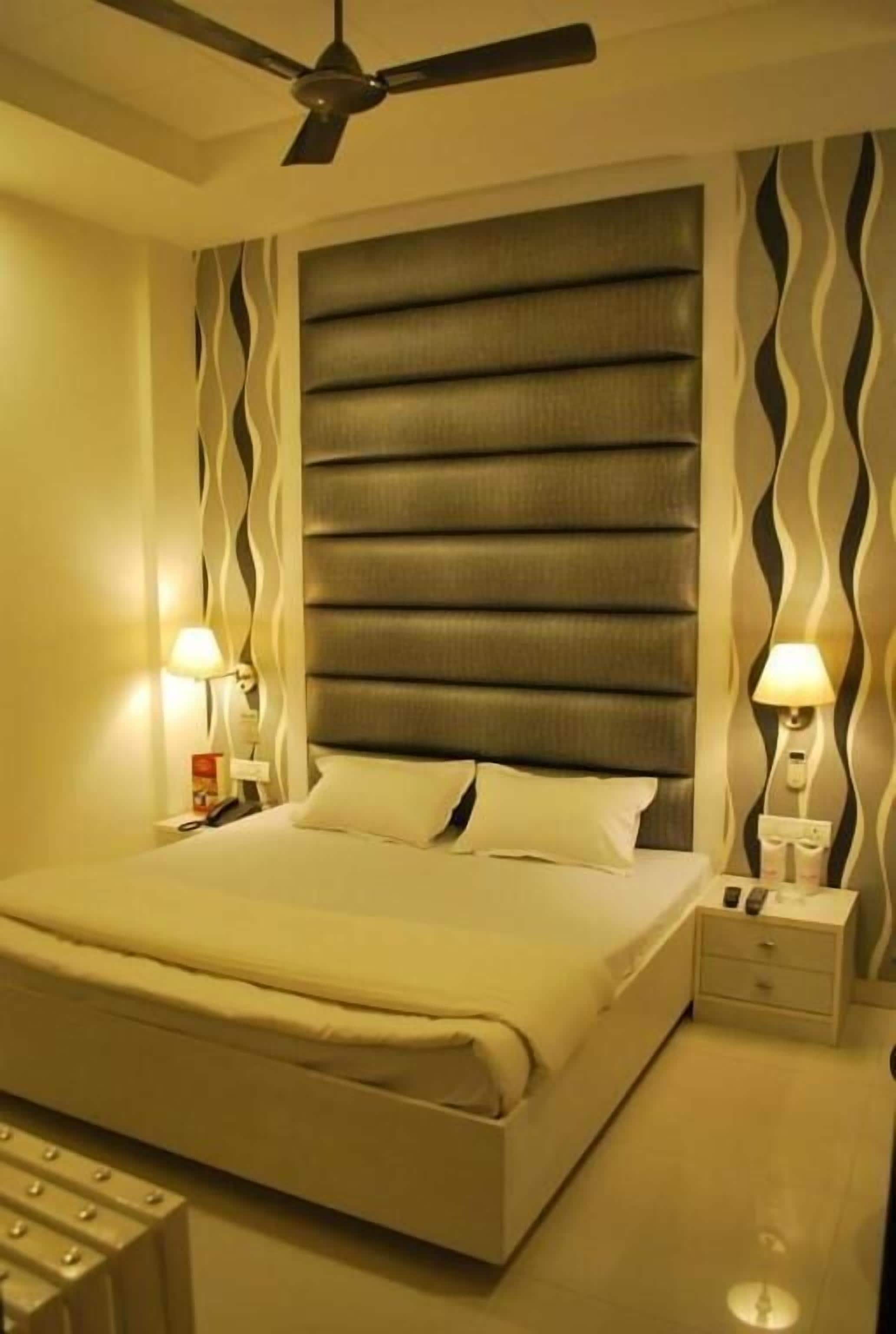 A hotel room with a large bed, a ceiling fan, and a modern design with wavy wall patterns.