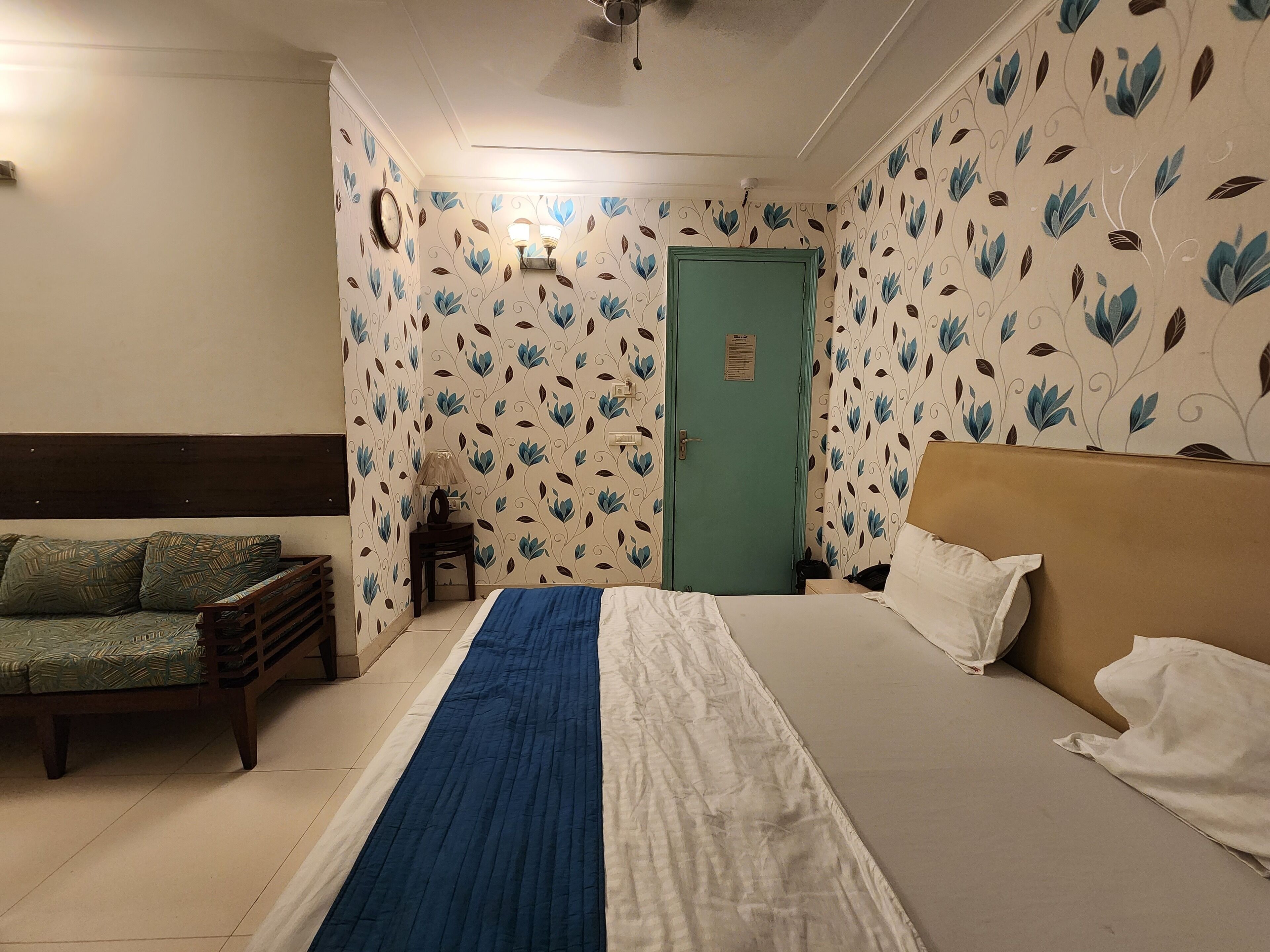 A hotel room with a bed, a sofa, a nightstand, and a door.