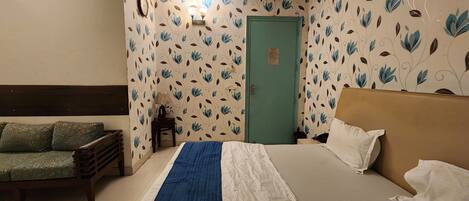 A hotel room with a bed, a sofa, a nightstand, and a door.