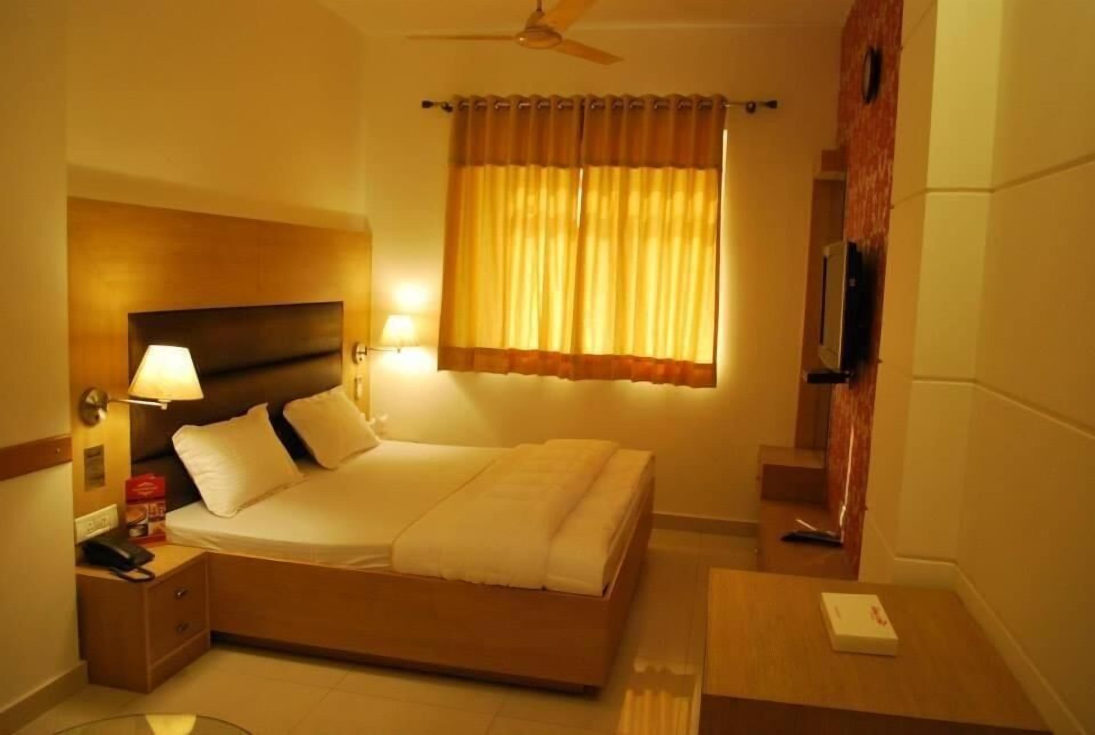 A hotel room with a bed, bedside lamp, nightstand, and a TV.