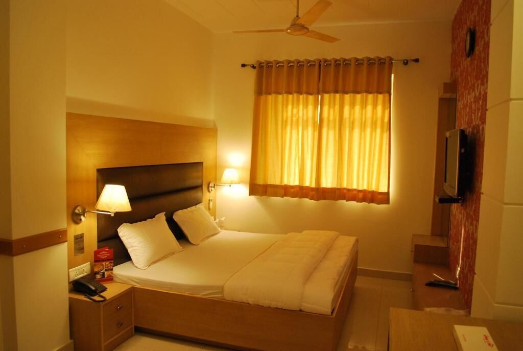 Quarto de hotel com cama, abajures, ventoinha no teto e janela com cortinas.