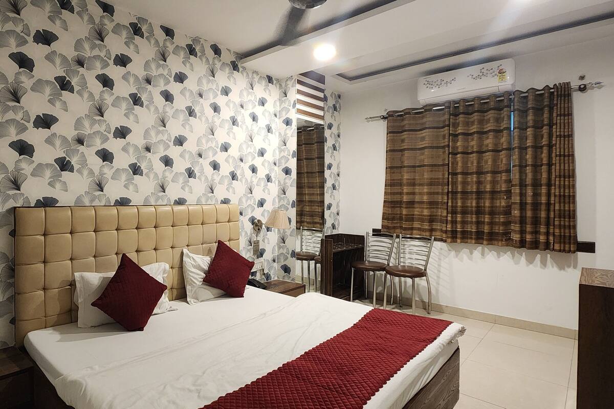 A hotel room with a bed, a headboard, a bedside table, a lamp, a desk, and a chair.
