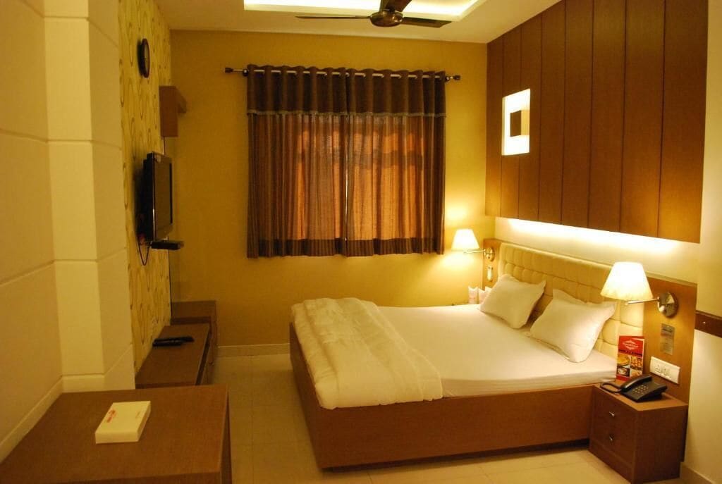 Habitación de hotel con cama, mesitas de noche, televisor y ventana con cortinas.