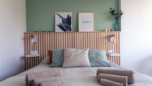 Un lit bien fait, agrémenté d’oreillers et de serviettes roulées, une tête de lit en bois avec des lattes verticales et des œuvres d’art encadrées accrochées au mur.