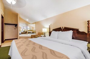 A hotel room with a large bed, a mirror, a bedside table, and a bathroom visible through the mirror.