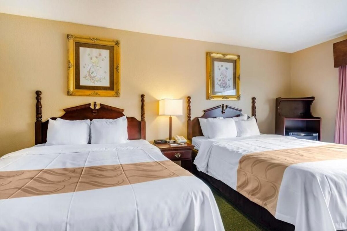 A hotel room with two beds, a nightstand with a lamp, and framed artwork on the walls.