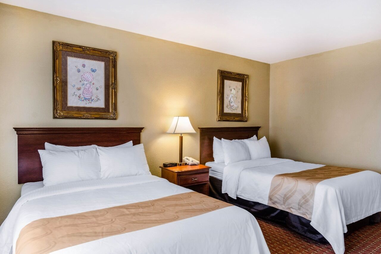 A hotel room with two beds, a nightstand with a lamp, and two framed pictures on the wall.