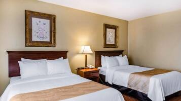 A hotel room with two beds, a nightstand with a lamp, and two framed pictures on the wall.