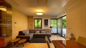 Un salon moderne avec un canapé d’angle, un plancher en bois et de grandes fenêtres donnant sur un paysage verdoyant.