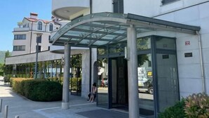 Un bâtiment moderne doté d’un auvent d’entrée en verre, d’un espace extérieur abrité avec des sièges et d’un ciel dégagé.