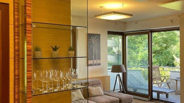 Un salon moderne avec une cloison en verre, un canapé, une table basse et un balcon aménagé avec du mobilier d’extérieur.