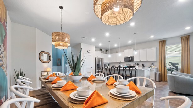 A modern dining area with a long wooden table, white chairs, and orange napkins.