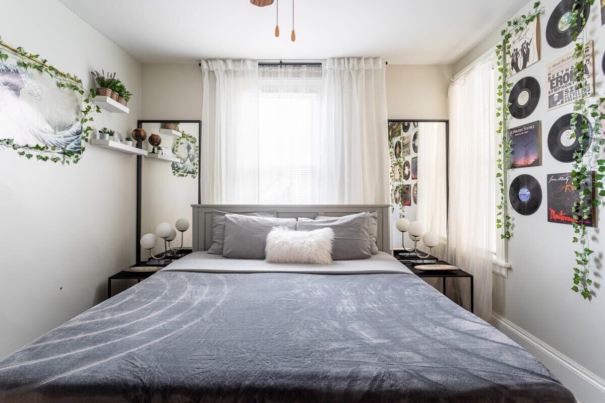 A bedroom with a bed, bedside tables, a mirror, and wall decorations including vinyl records and plants.