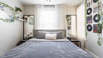 A bedroom with a bed, bedside tables, a mirror, and wall decorations including vinyl records and plants.