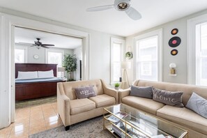 En moderne stue med sofa, sofabord og en seng i baggrunden.