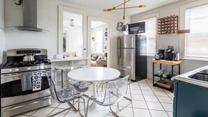 Una cucina moderna con piano cottura in acciaio inossidabile, frigorifero e zona pranzo con tavolo bianco e sedie trasparenti.