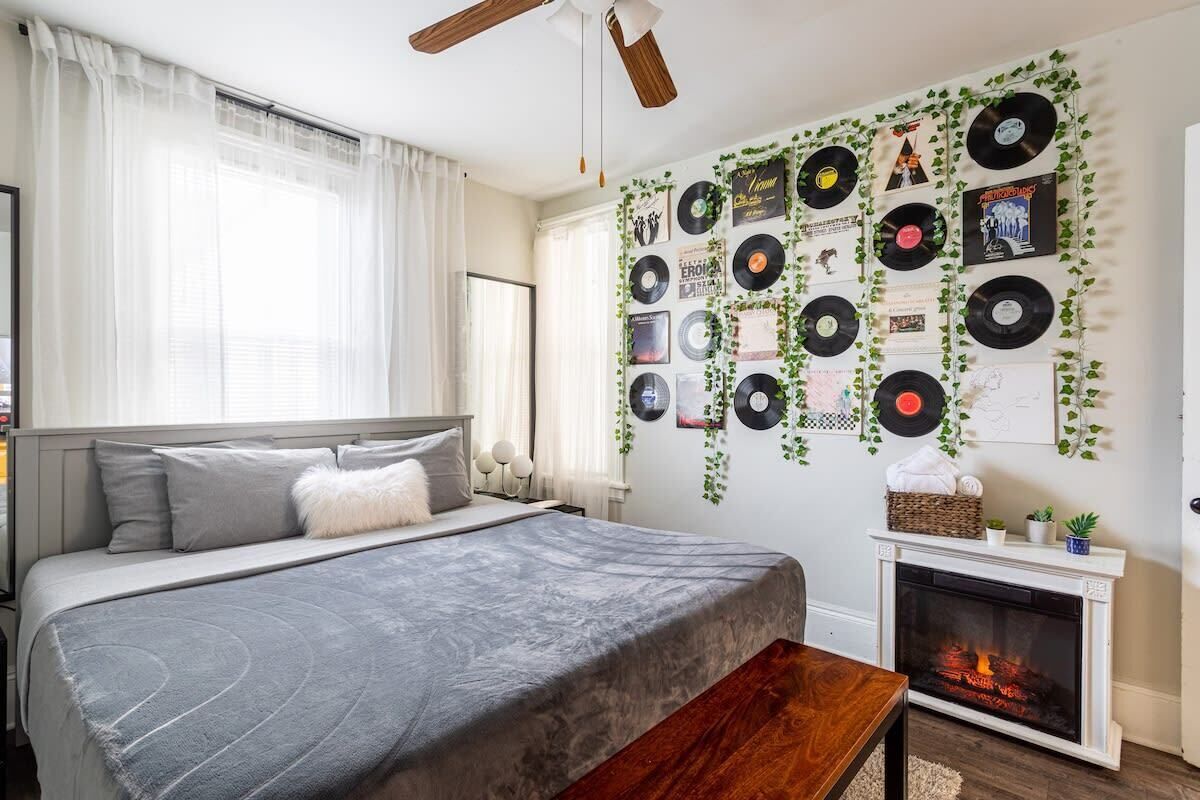 Une chambre à coucher comprenant un lit, une table de chevet, une cheminée et un mur décoré de disques vinyles et de plantes.