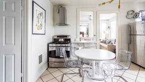 Una cucina moderna con piano cottura a gas, forno e frigorifero in acciaio inossidabile. Si nota un tavolo da pranzo bianco con sedie trasparenti e un lampadario a soffitto in vetro.