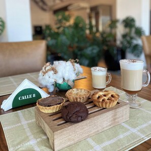 Une table avec un plateau de viennoiseries, une tasse de café et un verre de café.