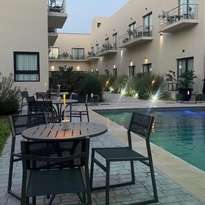 Un espace aménagé au bord de la piscine, avec des sièges extérieurs, une piscine et un bâtiment doté de balcons.