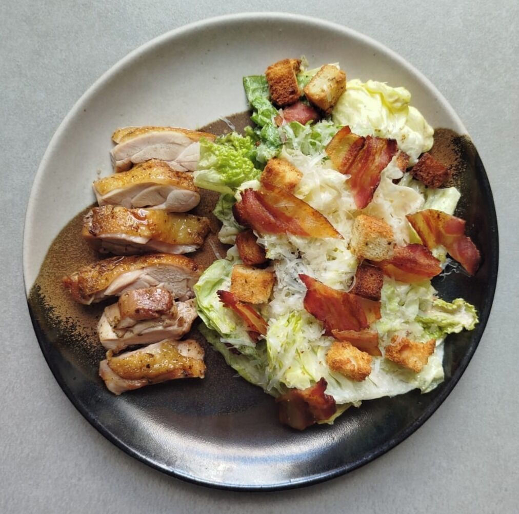 A plate with sliced meat, croutons, and lettuce.